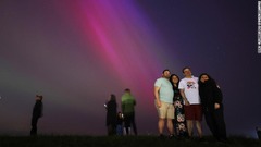 北のオーロラを背景に写真撮影のポーズを取る人々＝１０日、英イングランド・クロスビー