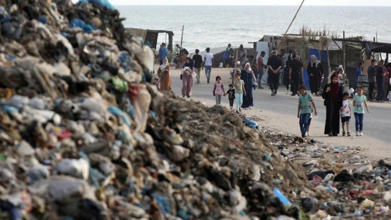 ガザ中部のデイルアルバラで、ゴミの山のそばを歩く人々＝５月２６日撮影/Ashraf Amra/Anadolu/Getty Images